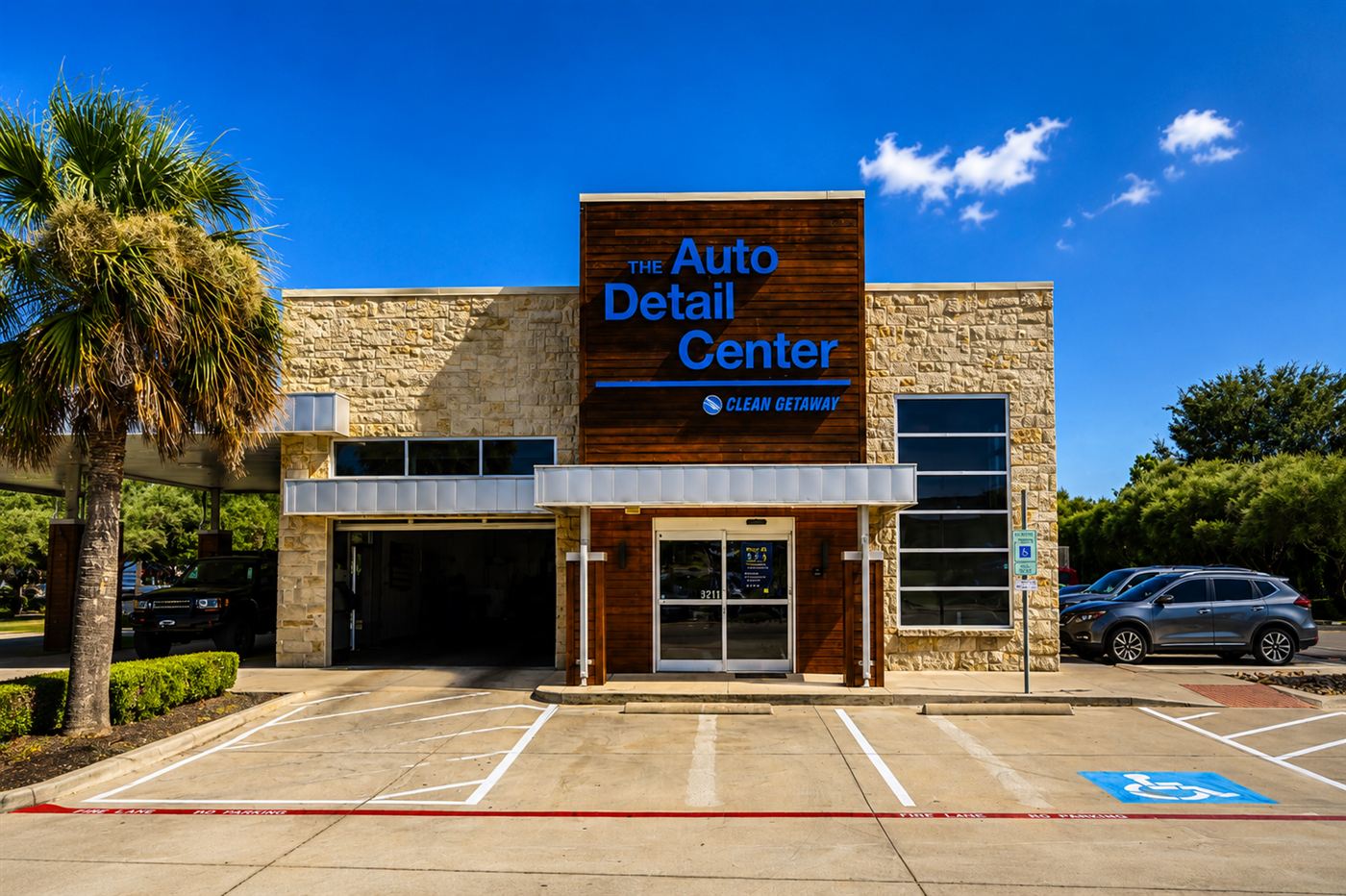 The Auto Detail Center building — stone and wood facade with blue signage, open bay door, and palm trees under a blue sky