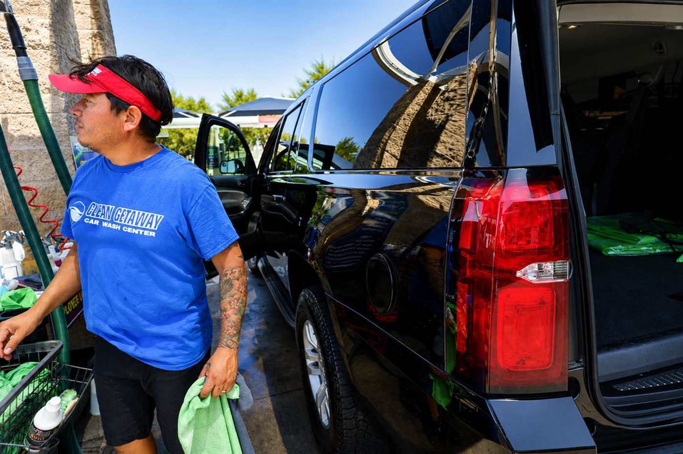 Crew member in a red visor giving a black SUV its final wipe-down