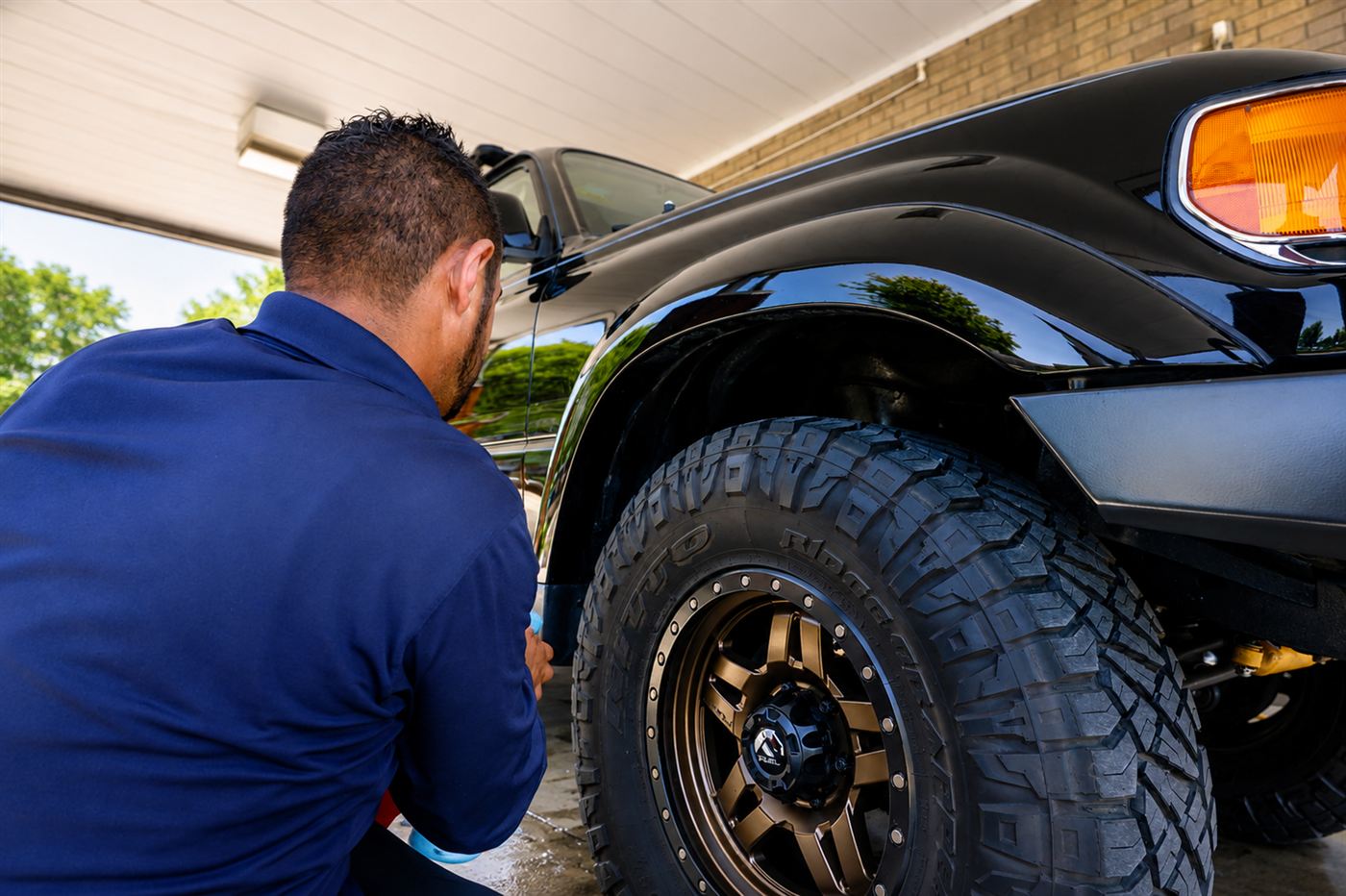 Detailer hand-cleaning the wheel and tire of a lifted black truck